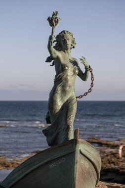Rota, Cadiz, Spain; 06/10/2025: Freedom Monument in Rota, Cadiz, Spain. Bronze sculpture of a woman breaking free from chains, standing on a boat named Libertad, by the seaside under clear sky