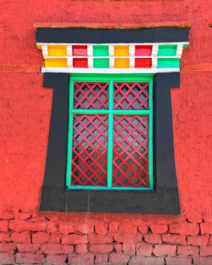 Kırmızı kafes ve turkuaz çerçeveli canlı bir Tibet penceresi, desenli kırmızı bir duvarda. Çıtır çıtır, ticari, mimari ve tasarım odaklı kullanım için ideal
