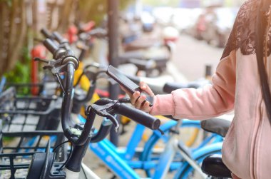 İnsanlar QR kodunu açmak için paylaşılan bir bisikletin üzerinde akıllı telefon kullanırlar..