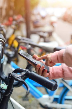 İnsanlar QR kodunu açmak için paylaşılan bir bisikletin üzerinde akıllı telefon kullanırlar..