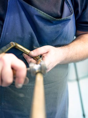 Uzman teknisyen bir müzik aleti tamir atölyesinde bir trombonun kaydırağını öğütüyor.