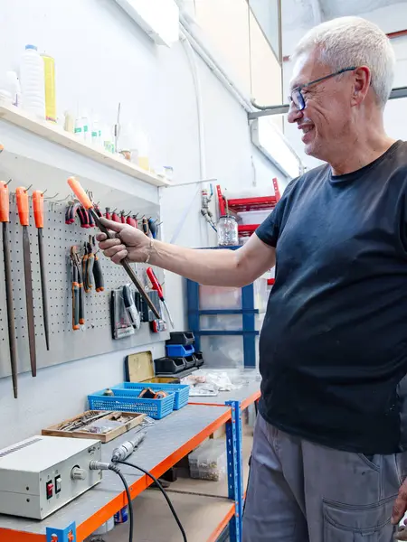 Pirinçten müzik aleti tamirhanesindeki bir panelden dosya alan bir Luthier 'ın genel görüntüsü.