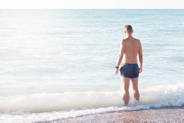 Sahilin kıyısındaki genç adam geriye doğru denize bakıyor.