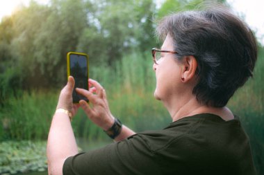 Kadın cep telefonuyla doğayı fotoğraflıyor.