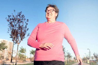 Sağlık, kardiyo ve dayanıklılık gelişimi için şehir parkında koşan yaşlı bir kadının yakın çekimi..