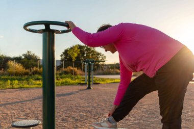 Spor giyim bölümündeki yaşlı bayan sonbaharda parktaki bir sokak sporları sahasında jimnastik barlarının yanında esneme hareketleri yapıyor. Vücut spor sahasında spor yapmak için spor ve kardiyo egzersizleri..