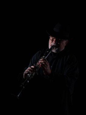 Beyaz sakallı, yuvarlak gözlüklü, müzik gününde müzik yapan, el yapımı Mısır flütü takmış siyah bir piyanonun önünde şapka takan yaşlı bir yetişkin. Siyah arka plan. Alçak tuş