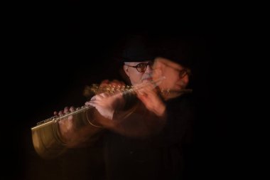 Beyaz sakallı, yuvarlak gözlüklü, müzik gününde müzik yapan, el yapımı Mısır flütü takmış siyah bir piyanonun önünde şapka takan yaşlı bir yetişkin. Siyah arka plan. Alçak tuş
