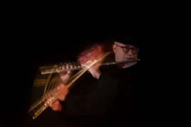 Beyaz sakallı, yuvarlak gözlüklü, müzik gününde müzik yapan, el yapımı Mısır flütü takmış siyah bir piyanonun önünde şapka takan yaşlı bir yetişkin. Siyah arka plan. Alçak tuş