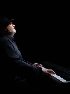 Beyaz sakallı, yuvarlak gözlüklü, müzik gününde müzik yapan, el yapımı Mısır flütü takmış siyah bir piyanonun önünde şapka takan yaşlı bir yetişkin. Siyah arka plan. Alçak tuş