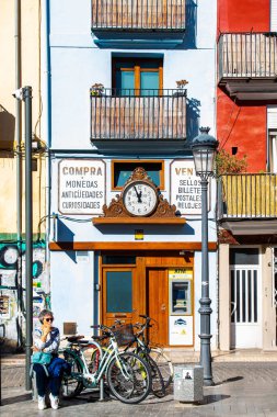 Valencia, İspanya - 19 Kasım 2023: İspanya 'nın tarihi merkezinde bisiklet kullanan yaşlı bir kadın. Arka planda antikacı dükkanı olan tipik bir yer. Güneşli bir gün