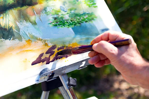 close-up detail of the watercolour painter painting a watercolour painting with a brush on an easel. Selective focus