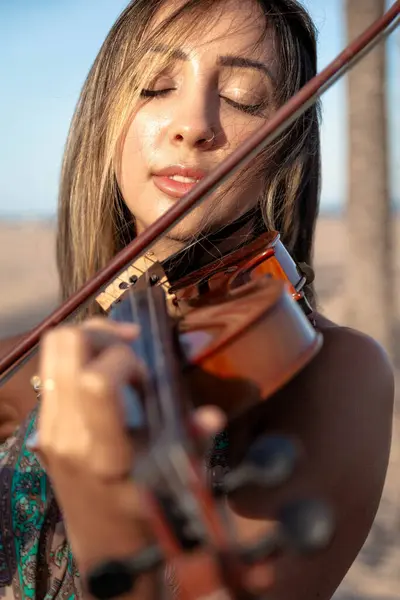 Woman violinist playing violin standing on the beach on the sand with the sea in the background. Close-up. Sunny afternoon