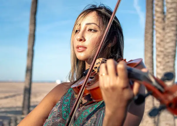 Woman violinist playing violin standing on the beach on the sand with the sea in the background. Close-up. Sunny afternoon