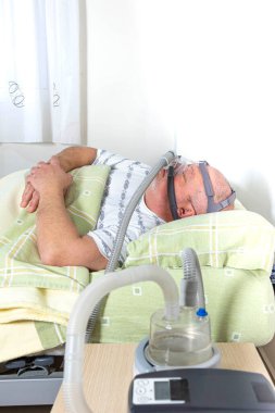Bir pulmonolog tarafından uyku apnozisi problemleri için teşhis edilen CEPAP (sürekli pozitif hava yolu basıncı) makinesi kullanarak yatakta uyuyan erkek.
