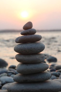 Bulanık gün batımına karşı deniz kıyısında taş yığını