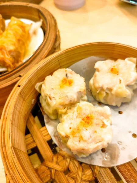 Karidesli tavuk köfteleri bambu kaplarda servis edilir, geleneksel Çin yemeği izlenimi verir, ahşap bir masada servis edilir..