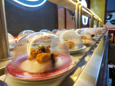 Surabaya, Doğu Java, Endonezya, 5 Mayıs 2024. Suşi menüleri bir suşi servis masasında servis edilir. Lokantalar boyunca uzanan bir tabakta istedikleri yemeği seçebilirler..