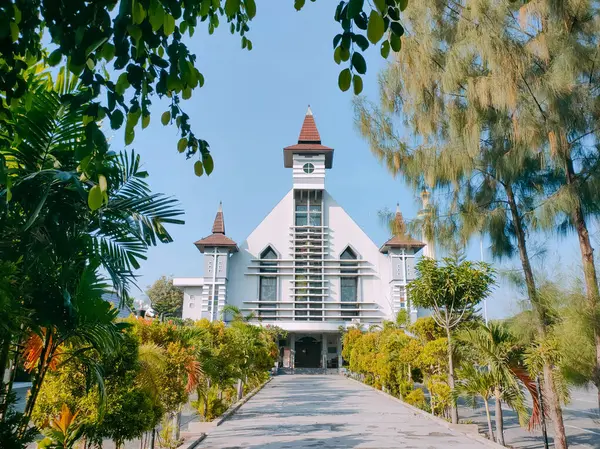 stock image Surabaya-Indonesia, May 18, 2024.Front view of an Indonesian tropical style Catholic Church. Photographed on a sunny morning, foliage in the foreground. Eye level view.