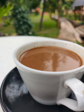 Sabah atmosfer yemyeşil bir bahçenin arka planında sütlü bir kahvenin tadını çıkarıyor. Bulanık Arkaplan.