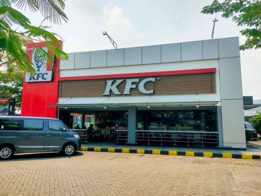 Surabaya - Endonezya, 18 Nisan 2024.Paralı yol dinlenme yerindeki kırmızı ve beyaz tabelalı bir KFC restoranının önü. Bina ağaçlarla çevrili ve bir otoparkı var..