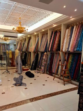 Surabaya - Endonezya, 18 Mart 2025. Bir kumaş mağazasındaki raflarda, ziyaretçilerin seçmesini kolaylaştırmak için sıra sıra kumaş ruloları sergileniyor. Göz düzeyi görünümü.