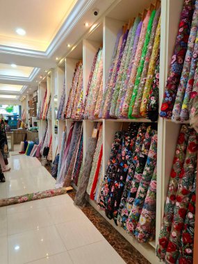 Surabaya - Endonezya, 18 Mart 2025. Bir kumaş mağazasındaki raflarda, ziyaretçilerin seçmesini kolaylaştırmak için sıra sıra kumaş ruloları sergileniyor. Göz düzeyi görünümü.
