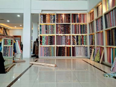 Surabaya - Endonezya, 18 Mart 2025. Bir kumaş mağazasındaki raflarda, ziyaretçilerin seçmesini kolaylaştırmak için sıra sıra kumaş ruloları sergileniyor. Göz düzeyi görünümü.