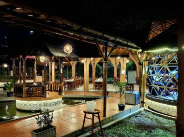 Sidoarjo - Endonezya, 19 Nisan 2025. Artistik bambu malzemeleriyle modern Endonezya geleneksel konseptiyle bir çardak yemek kompozisyonu. Gece dingin aydınlatmayla.
