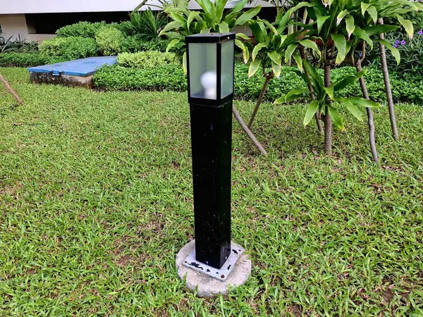 Kutu şeklinde bir bahçe ışığı, bitkilerin arasına yerleştirilmiş, aynı zamanda bir bahçe elementi..