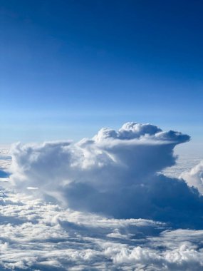 Uçak penceresinden beyaz kabarık bulutlu mavi gökyüzü manzarası
