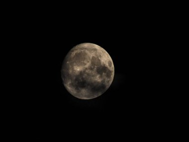 Dolunaya yakın plan gece Ay yüzeyinin detaylarını gösteriyor. Önplanda bulutlar.