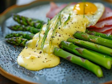 Bir tabakta Hollandaise soslu ve jambonlu kuşkonmaz.