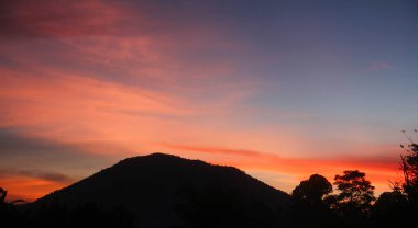 Tepelerin siluetleri ve tropikal yağmur ormanlarında yetişen birkaç ağacın olduğu bir dağda gün doğumları.