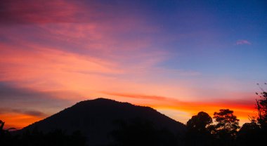 Güneş parlak dağlık bir alanda yükseliyor, görünen tepeler ve ağaçların gölgeleri.