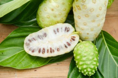 Noni meyvesi veya Morinda citrifolia dilimlenmiş ve doğal bir arka planda meyve ve yapraklarla süslenmiş.