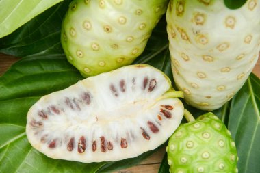 Noni meyvesi veya Morinda citrifolia dilimlenmiş ve doğal bir arka planda meyve ve yapraklarla süslenmiş.