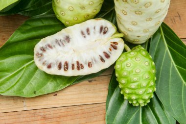 Noni meyvesi veya Morinda citrifolia dilimlenmiş ve doğal bir arka planda meyve ve yapraklarla süslenmiş.