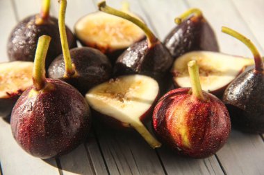 Taze ve doğranmış incirler beyaz ahşap bir masada, yiyecek arka planında.
