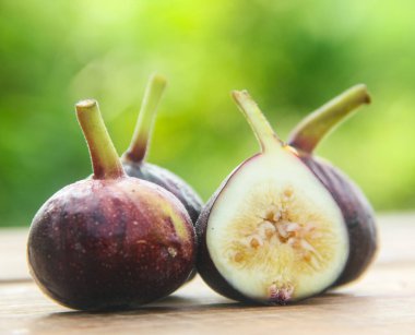 Taze incir, taze incir. Masada taze incir ve güneş ışığına maruz kalan yaprakların doğal arkaplanı.