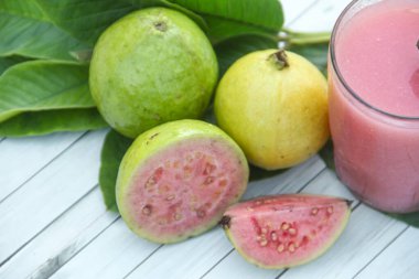 Guava suyu, cam bardakta taze guava suyu ve dokulu ahşap bir arka planda dilimlenmiş guava.