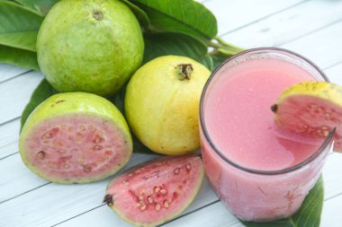 Guava suyu, cam bardakta taze guava suyu ve dokulu ahşap bir arka planda dilimlenmiş guava.