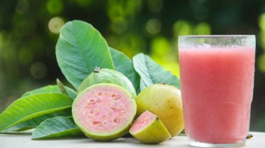 Guava suyu, cam bardakta taze guava suyu ve doğal arka planda guava dilimleri.