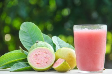 Guava suyu, cam bardakta taze guava suyu ve doğal arka planda guava dilimleri.