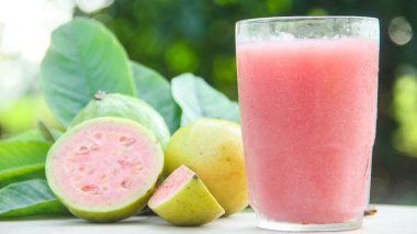 Guava suyu, cam bardakta taze guava suyu ve doğal arka planda guava dilimleri.