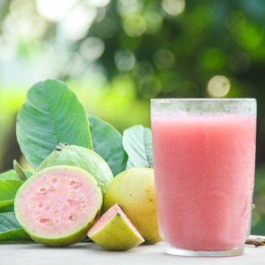Guava suyu, cam bardakta taze guava suyu ve doğal arka planda guava dilimleri.