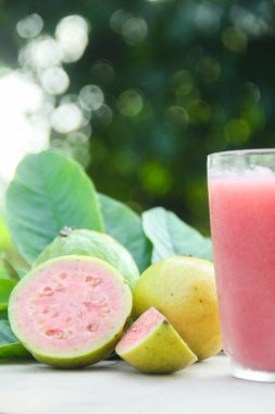 Guava suyu, cam bardakta taze guava suyu ve doğal arka planda guava dilimleri.
