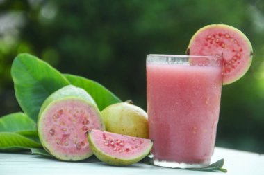 Guava suyu, cam bardakta taze guava suyu ve doğal arka planda guava dilimleri.