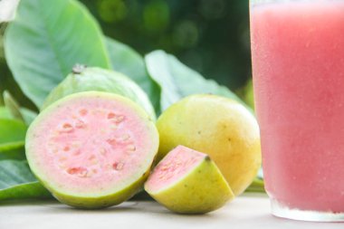 Guava suyu, cam bardakta taze guava suyu ve doğal arka planda guava dilimleri.