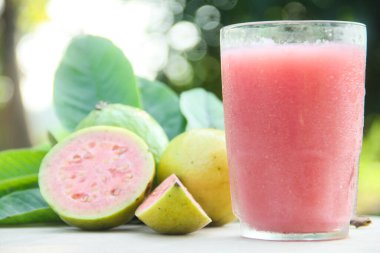 Guava suyu, cam bardakta taze guava suyu ve doğal arka planda guava dilimleri.